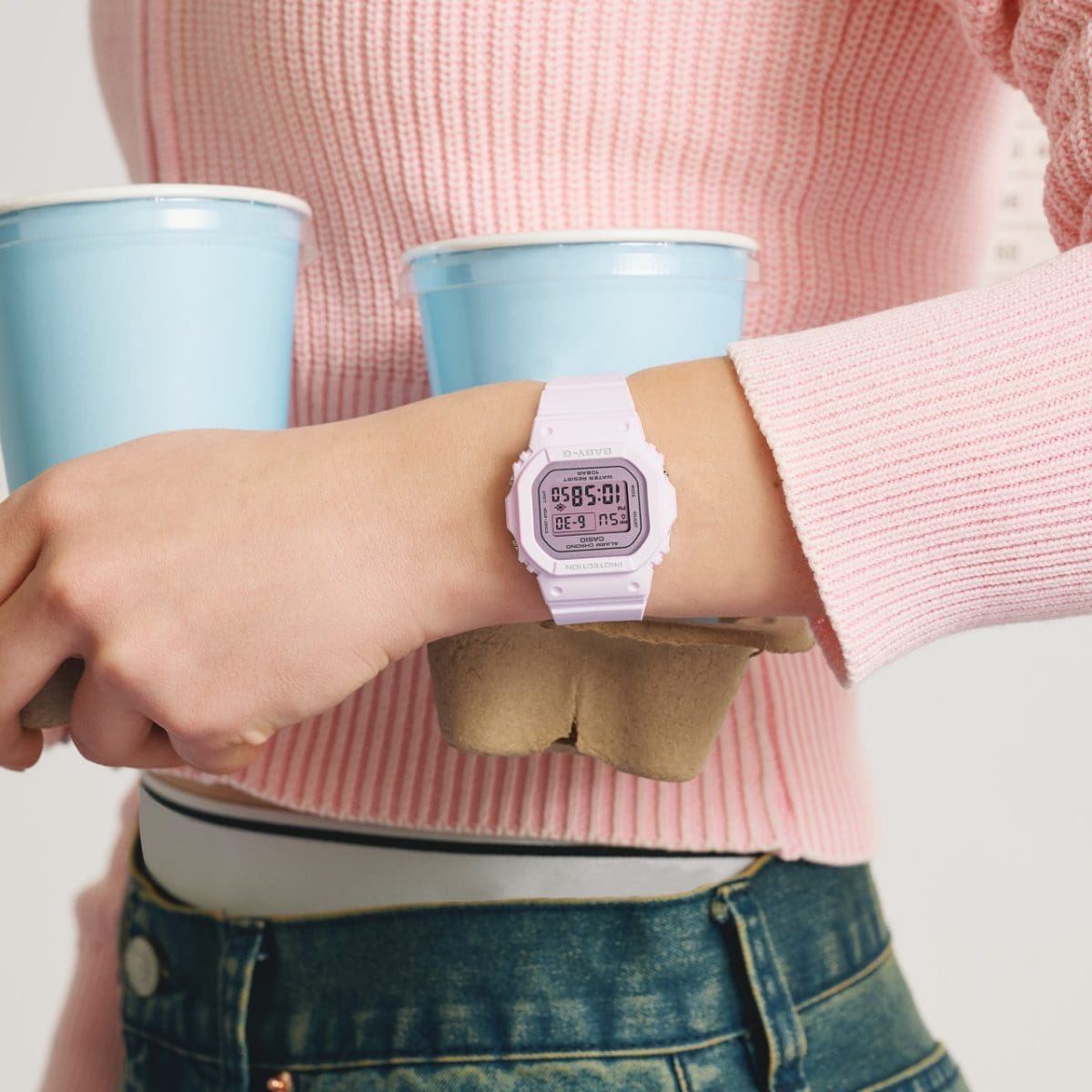 Une femme portant un haut rose transporte un porte-gobelet en carton contenant deux gobelets et porte la montre-bracelet BABY-G BGD-565SC-4BER à son poignet.