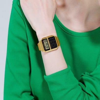 La montre-bracelet CASIO CA-500WEG-1A de couleur or sur le poignet d'une femme portant un t-shirt vert.
