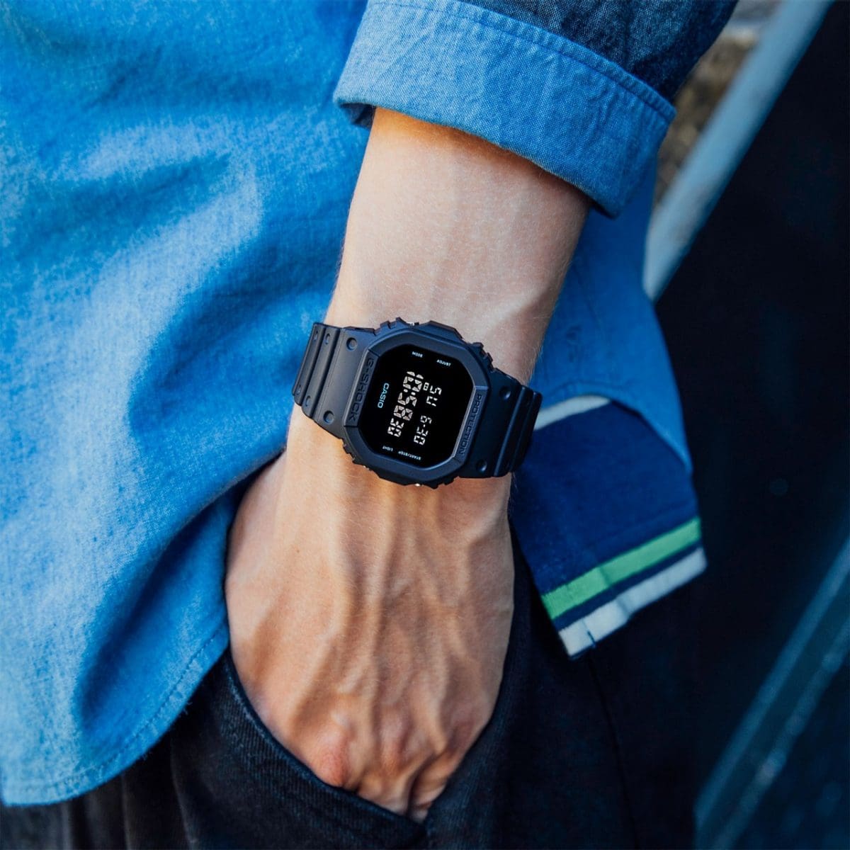 La montre digitale DW-5600UBB-1 montre digitale au poignet d'un homme qui met la main dans la poche de son pantalon.
