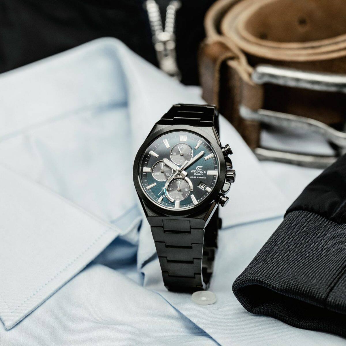 L'EFS-S630DC-2AV est posé sur une chemise bleu clair, son bracelet fermé. Une ceinture marron est visible en arrière-plan.