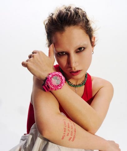 Une femme vêtue d'un haut rouge et ayant les cheveux courts porte à son poignet la montre-bracelet rose GA-V01CMG-4AER.