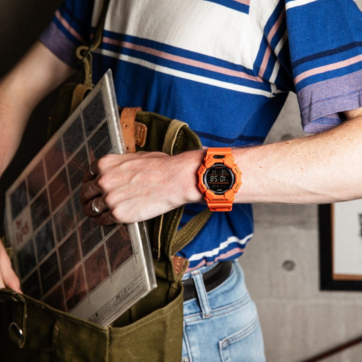 Un homme portant un jean, un t-shirt à rayures et la montre orange G-SHOCK GD-010-4 sort un disque de sa poche.