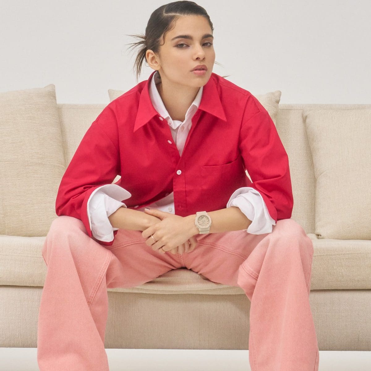 Une femme portant un haut rose et un pantalon rose est assise sur un canapé et porte le GMA-P2100M-4A beige à son poignet.