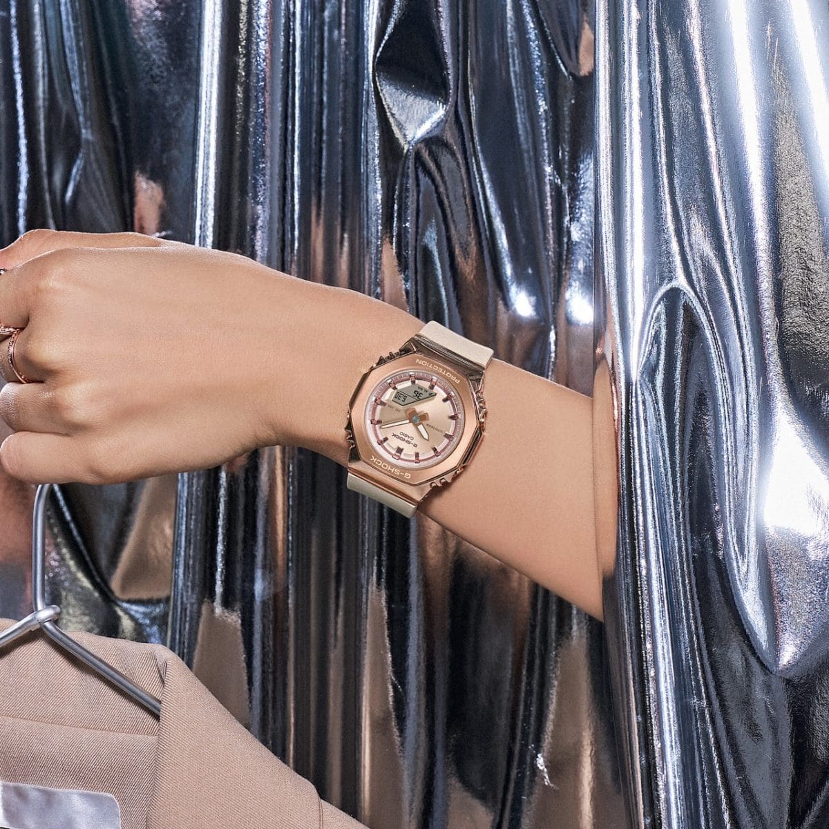 Gros plan sur la montre analogique rose-beige GM-S2110PG-4A au poignet d'une femme, dépassant d'un rideau métallique.
