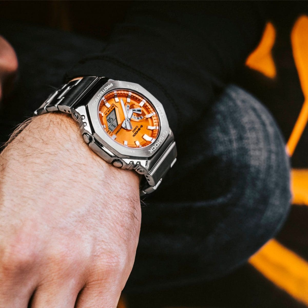 GM-2110D-4AER Full-Metal G-SHOCK avec bracelet argenté et cadran orange au poignet d'un homme