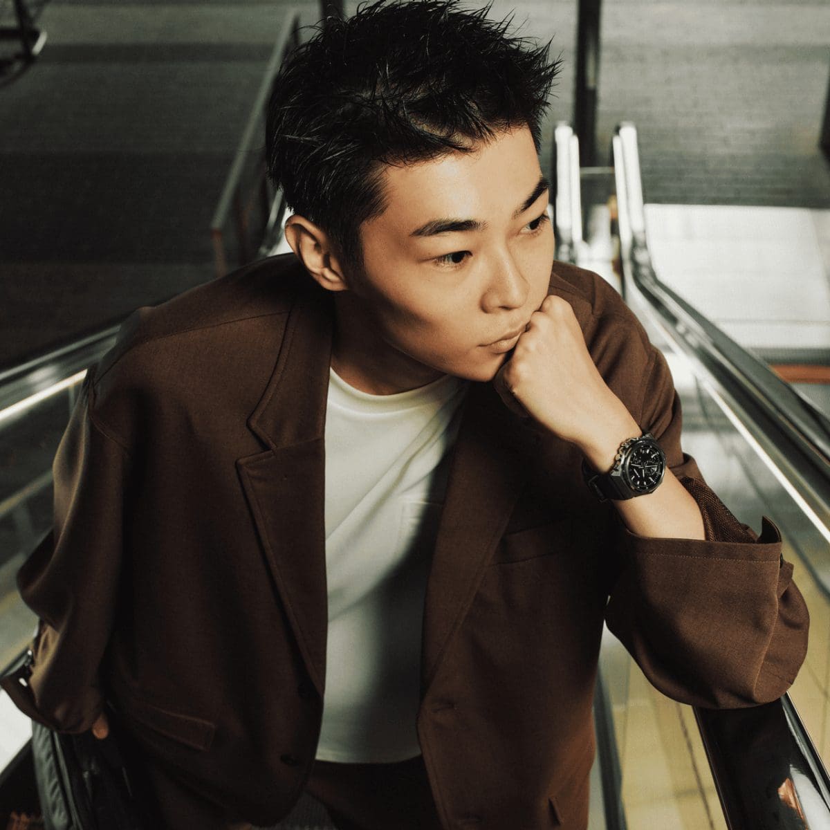 Un homme portant une veste marron se tient sur un escalator et porte une montre G-SHOCK GST-B1000-1AER au poignet.
