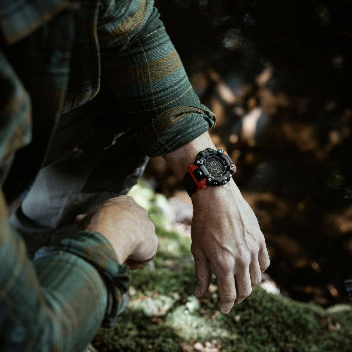 La montre GW-9500-1A4 au poignet d'un homme portant une chemise à carreaux verts. En arrière-plan, on peut voir le sol d'une forêt.