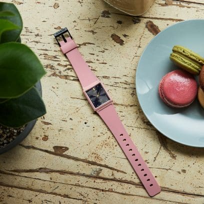 La montre MQ-38UC-2A2 posée à plat sur une table en bois à côté de macarons sur une assiette et d'une plante.
