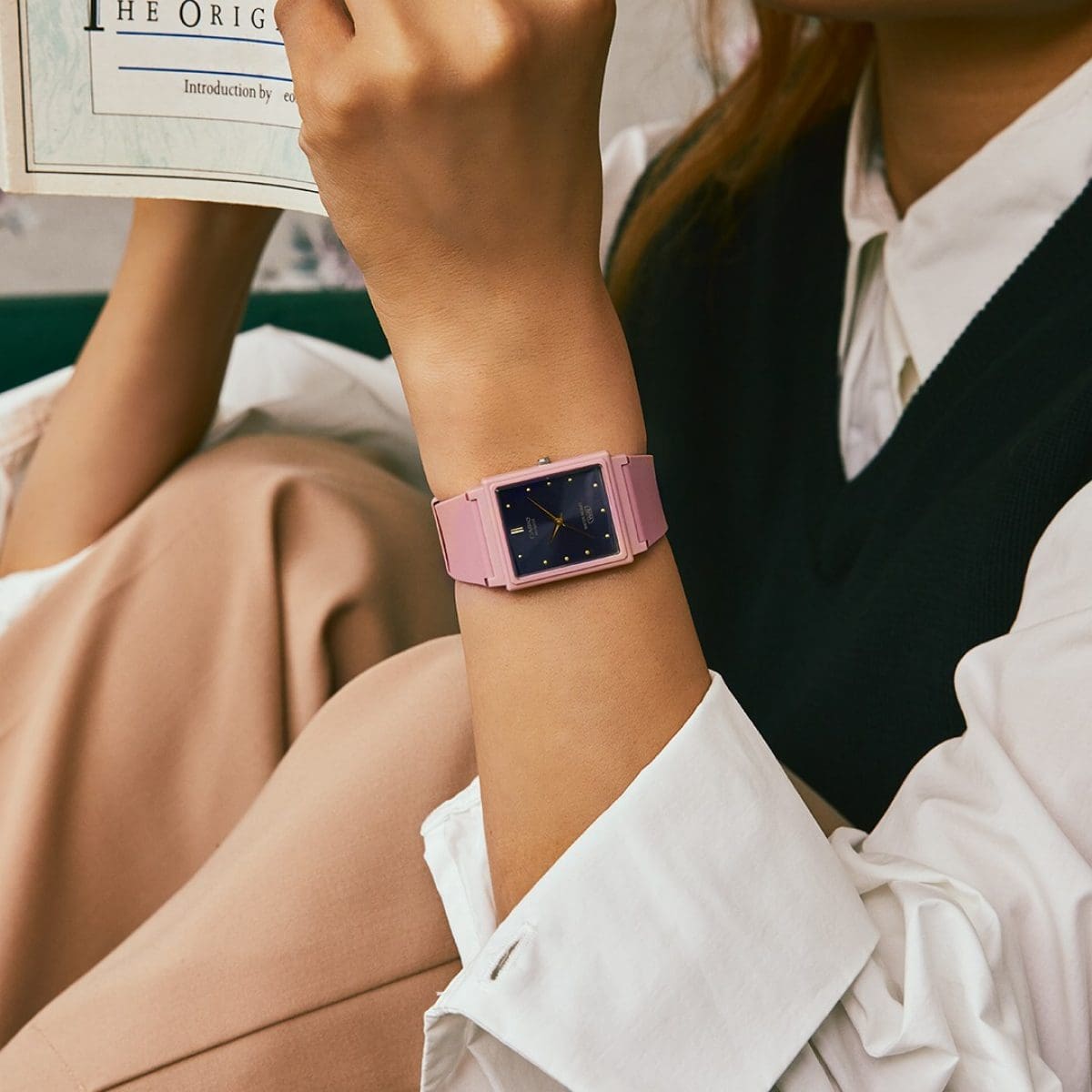 Gros plan sur le poignet d'une femme vêtue d'un chemisier blanc et d'un pull noir, qui lit un livre. Elle porte au poignet la montre analogique MQ-38UC-2A2.