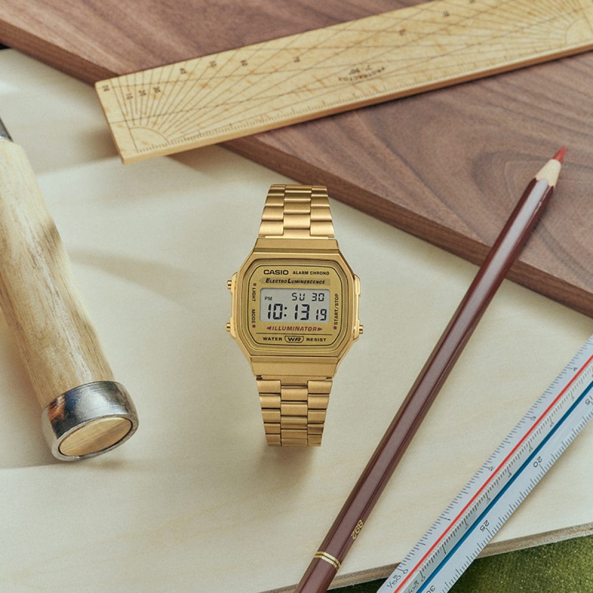 L’orologio CASIO Vintage A168WG-9, con cinturino metallico dorato e display digitale, posato accanto a strumenti e articoli da cancelleria.