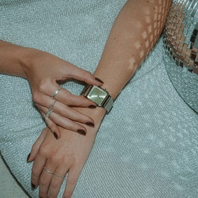 Una donna siede accanto a una palla da discoteca e preme i pulsanti del suo orologio da polso, il CASIO Vintage Collection AQ-230A-9AMQYES con lunetta verde chiaro 