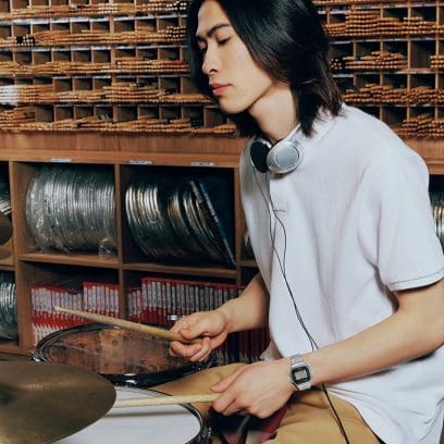 Un batterista che si esercita con le cuffie, indossando l’orologio digitale argento ABL-100WE-1A, in un ambiente pieno di musica.