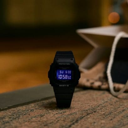 Il modello BGD-565U-1ER è posizionato su una superficie rocciosa davanti a uno sfondo illuminato da luci calde. Il display blu è acceso. 