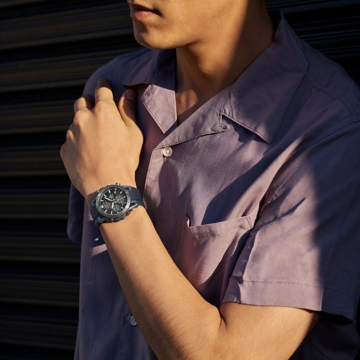 L'orologio da polso EDIFICE EFS-S640PB-1AV al polso di un uomo che indossa una camicia a maniche corte color lilla e si trova al sole.