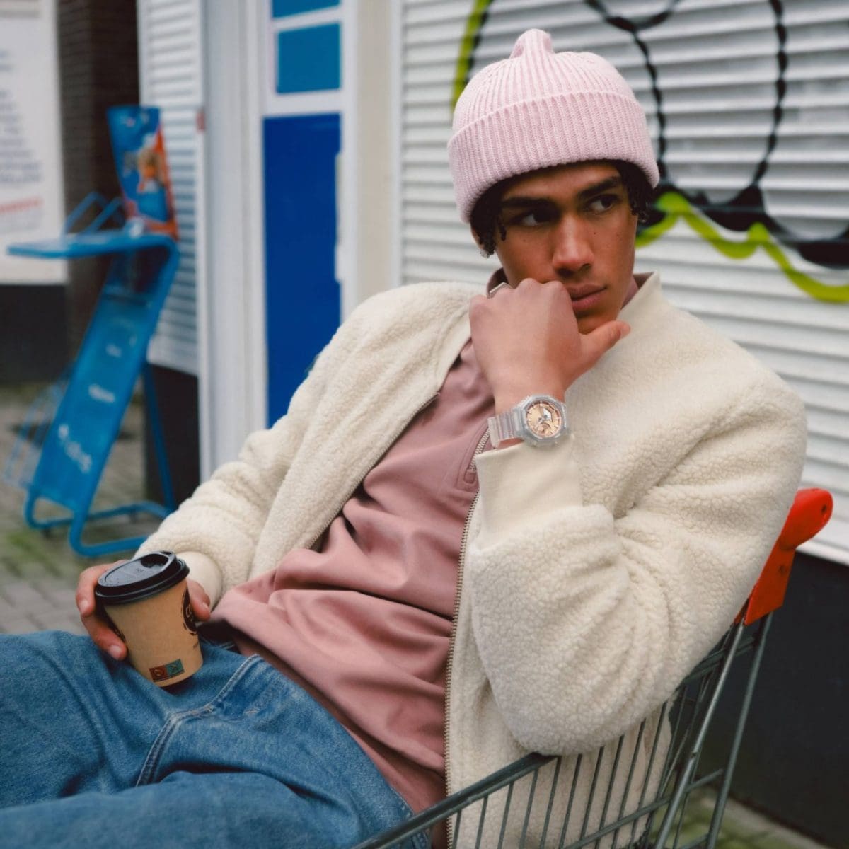 Il modello maschile è seduto su un carrello della spesa e indossa il modello GA-2100BM-7A5 abbinato a un outfit streetwear alla moda composto da berretto e maglietta color pastello e giacca bianca.