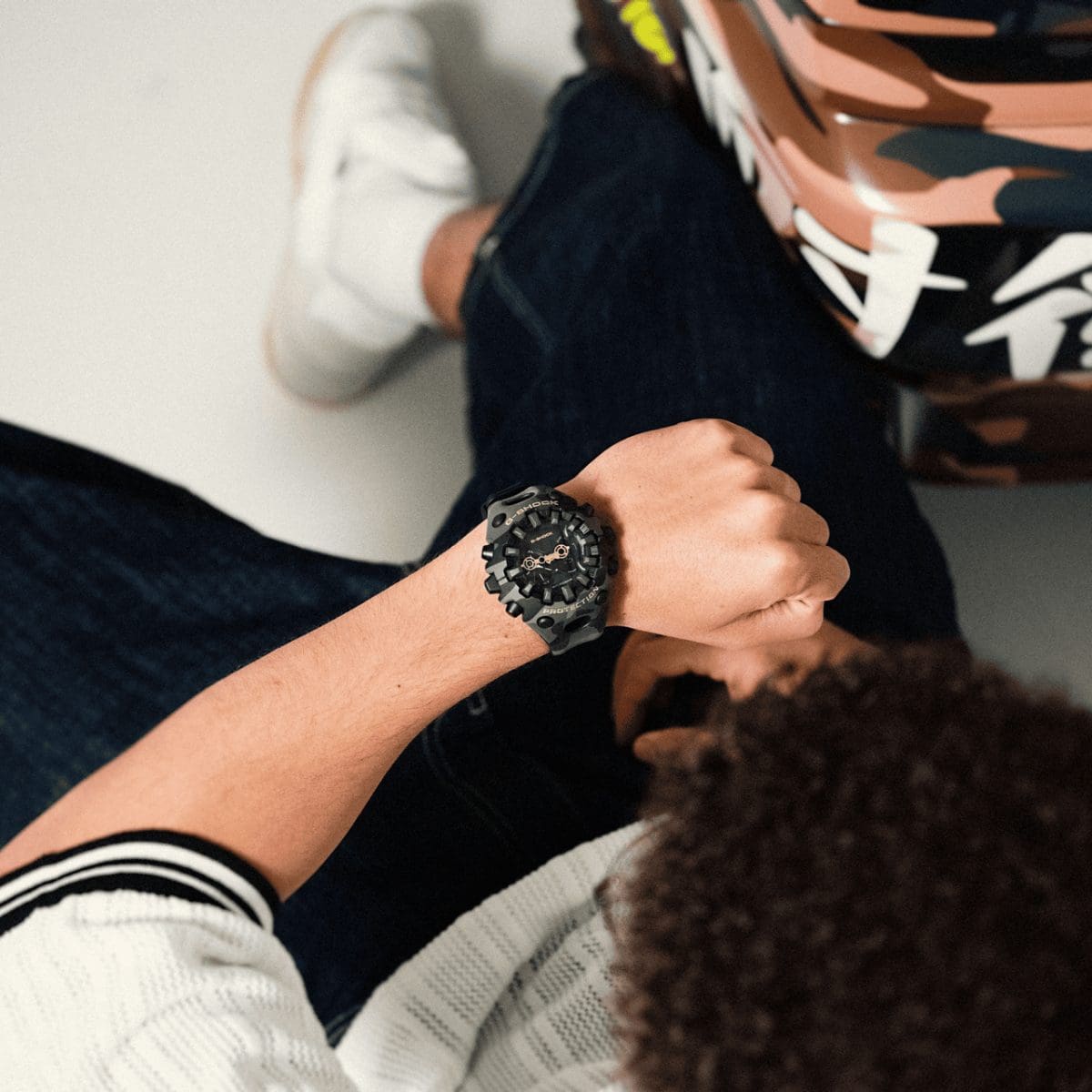 Un uomo in jeans guarda il proprio polso, dove indossa l'orologio da polso mimetico GA-V01CMG-3AER di G-SHOCK