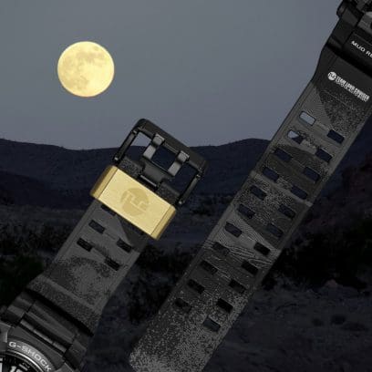 Sullo sfondo del bracciale nero con il ferma-cinturino dorato del MUDMASTER GWG-B1000TLC-1AER, si può vedere una luna piena nel cielo.