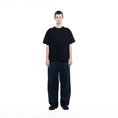 Een man in een donkere spijkerbroek draagt ​​een GXFAB T-shirt.
