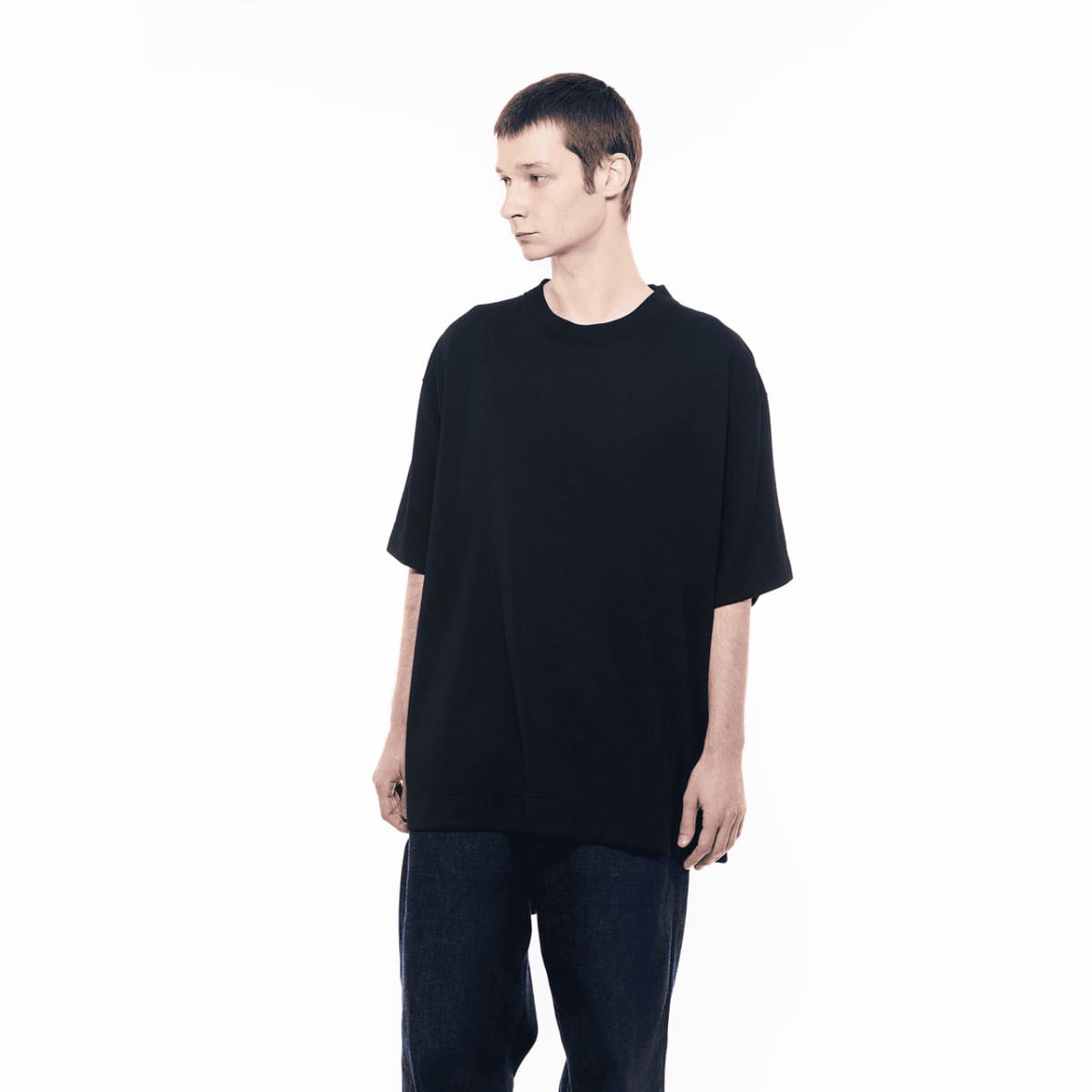 Een man in een donkere spijkerbroek draagt ​​een GXFAB T-shirt.