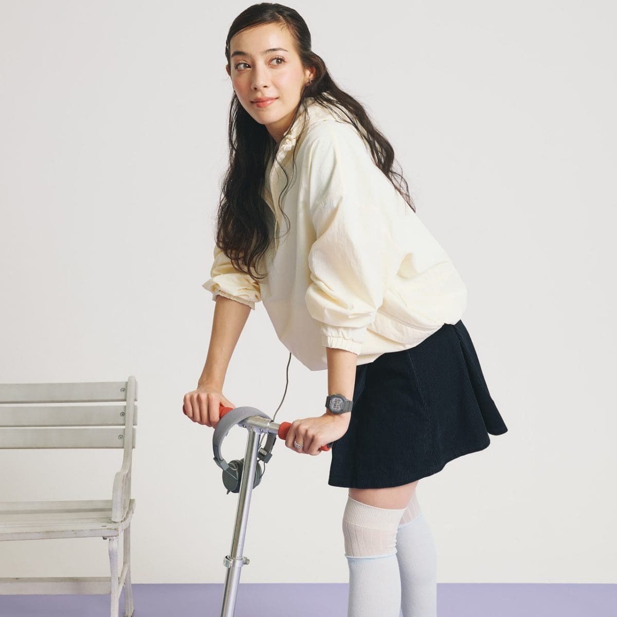 Een vrouw, gekleed in een donkere rok en een lichte trui, staat op een scooter en draagt ​​het BABY-G digitale horloge BGD-565SC-1ER om haar pols.