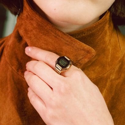 Een vrouw draagt ​​het CRW-001G-9ER-horloge op haar wijsvinger en draagt ​​een bruin suède jasje.