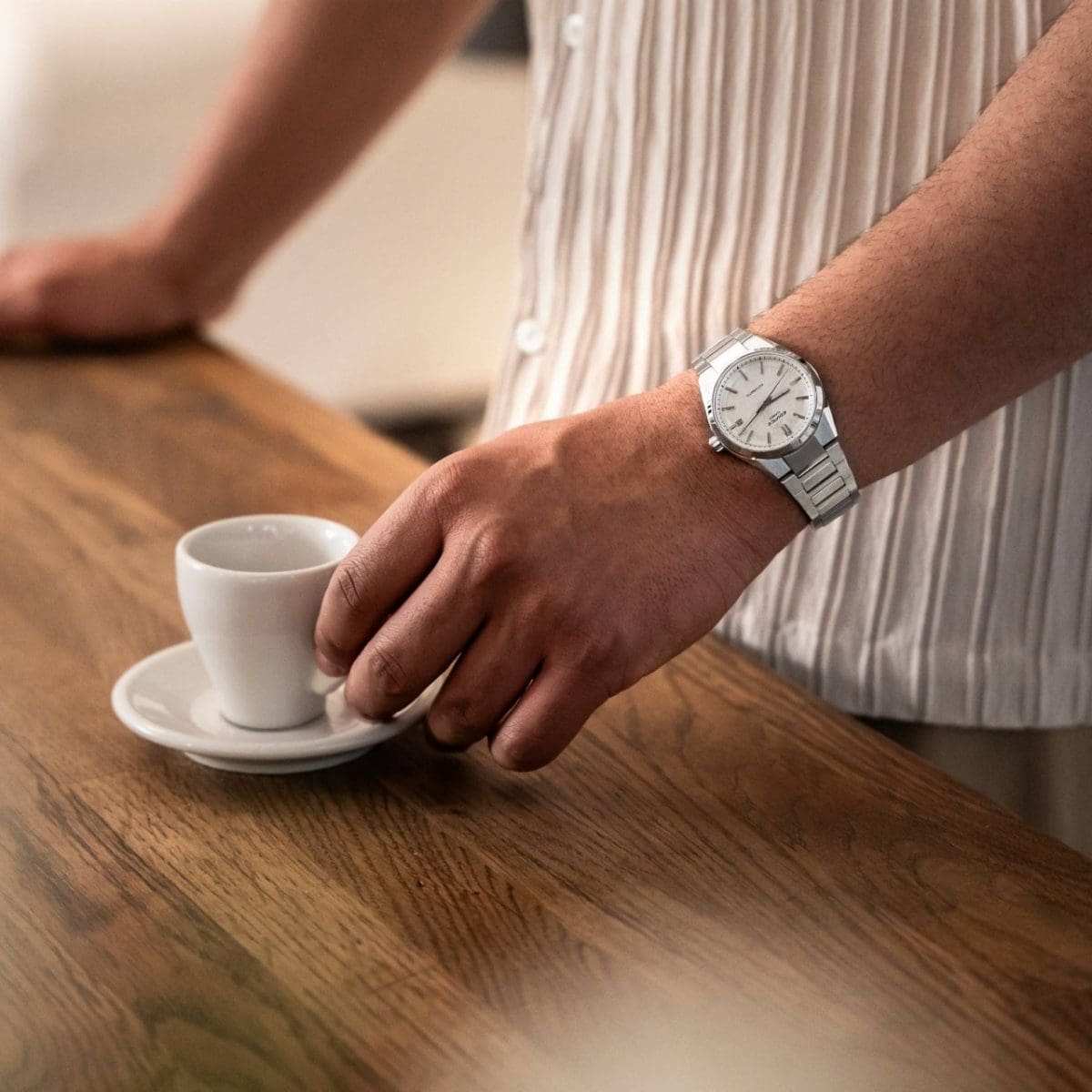 Een man in een beige shirt draagt ​​het mechanische EFK-110D-7A-apparaat om zijn pols en reikt naar een espressokopje