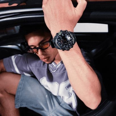 Een man met een zonnebril zit in de auto en draagt het horloge GA-V01CMG-3AER om zijn pols