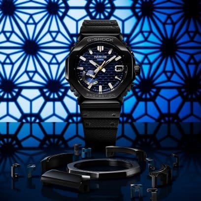 Het zwarte MRG-B2100R-2A analoge horloge met een donkerblauwe gedessineerde wijzerplaat tegen een blauw met zwart gedessineerde achtergrond