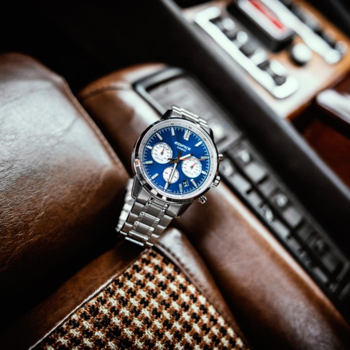O cronógrafo EDIFICE com luneta azul e bracelete metálica repousa no banco de um automóvel.