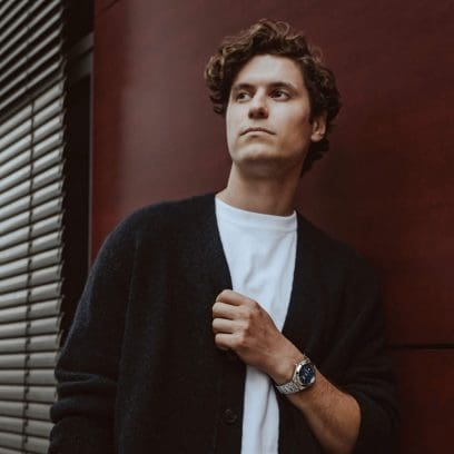 Um homem está usando o EFK-100D-2AER e está vestindo um cardigã preto sobre uma camiseta branca