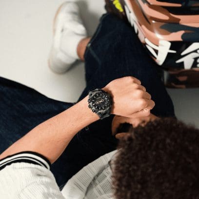 Um homem de calças de ganga olha para o pulso, onde usa o relógio de pulso Camouflage GA-V01CMG-3AER da G-SHOCK