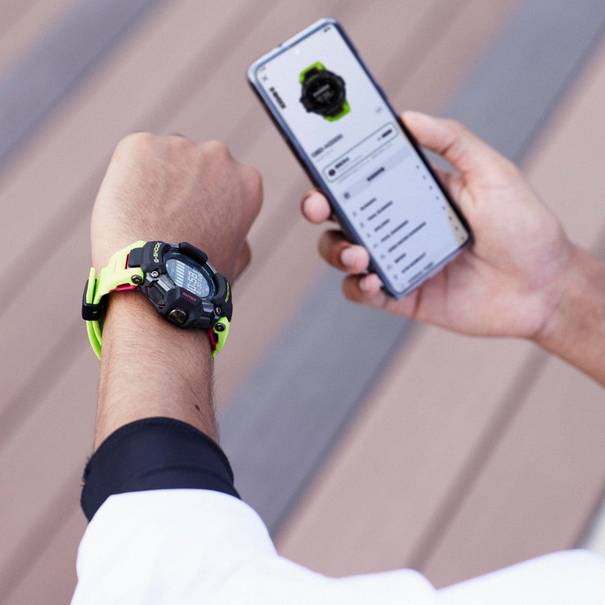 Uma pessoa usa o relógio multidesportos GBD-H2000-1A9 no pulso esquerdo enquanto segura um smartphone na mão direita, onde se podem ver os dados transmitidos pelo relógio