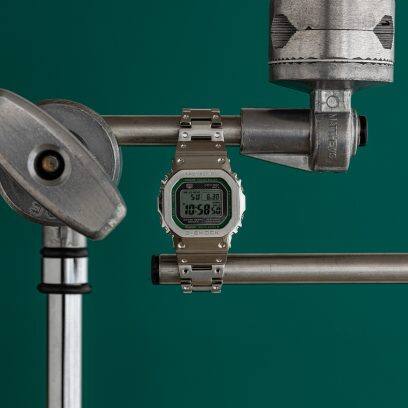 Vista frontal do GMW-B5000D-3 com pulseira fechada esticada em duas hastes de metal