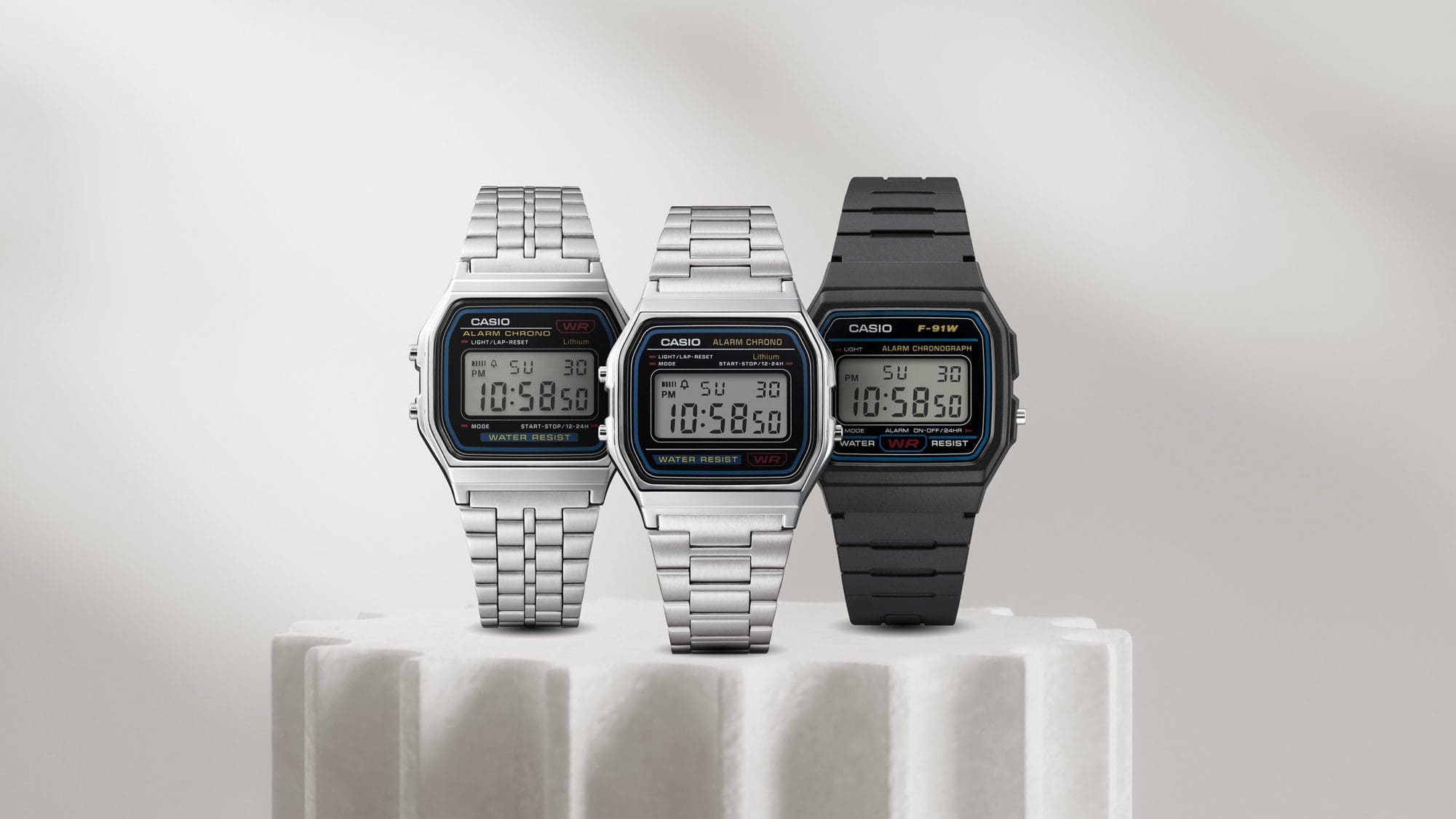 Drei unterschiedliche Modelle der F-91W und A158 von CASIO, mit silberfarbenem oder schwarzem Armband auf Podesten.