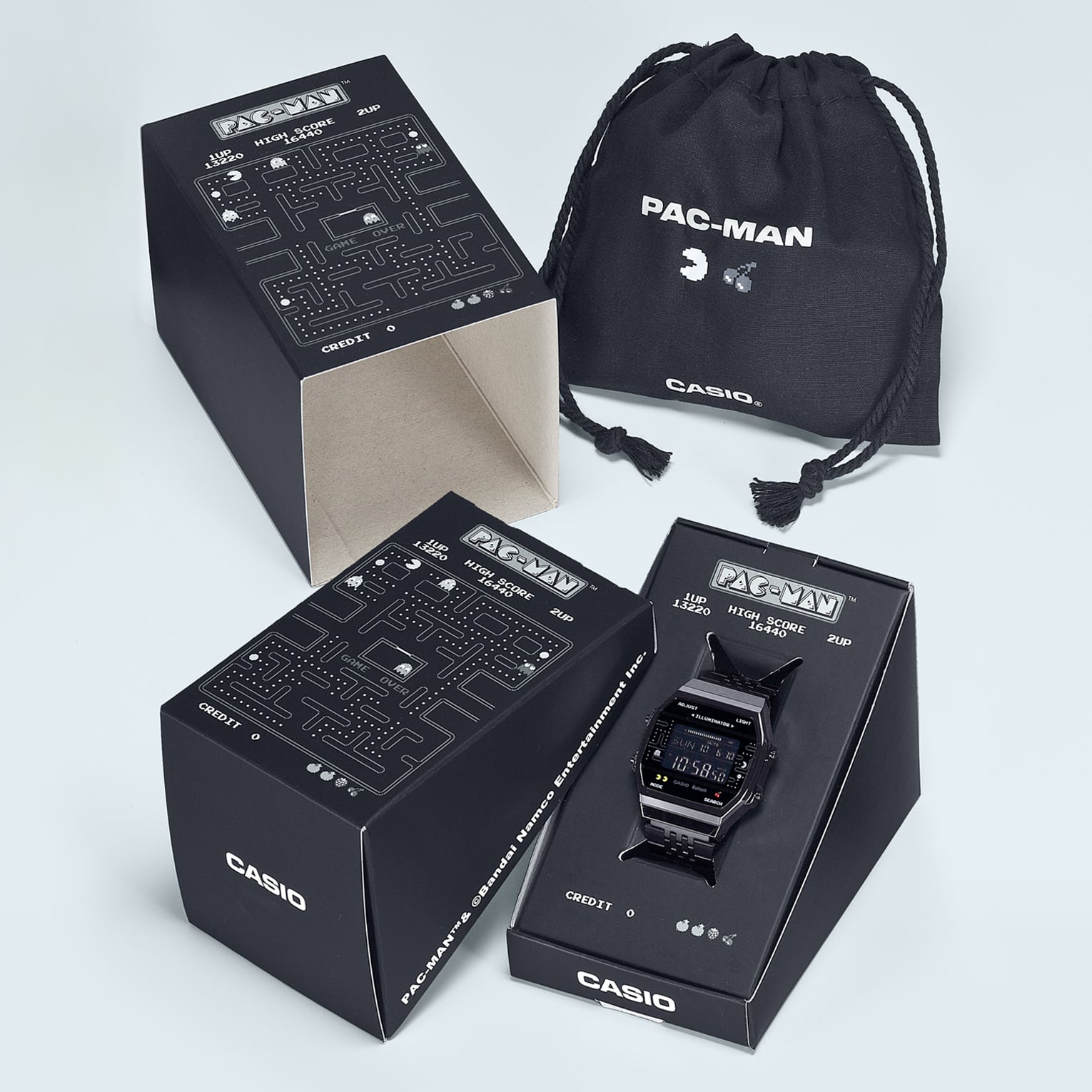 ABL-100WEPC-1B Die vierteilige Verpackung der schwarzen Pac-Man-Uhr ABL-100WEPC-1B bestehend aus Innenbox mit Deckel, Umverpackung und schwarzem Stoffbeutel,. Alle Teile sind mit Pac-Man-Motiven versehen.
