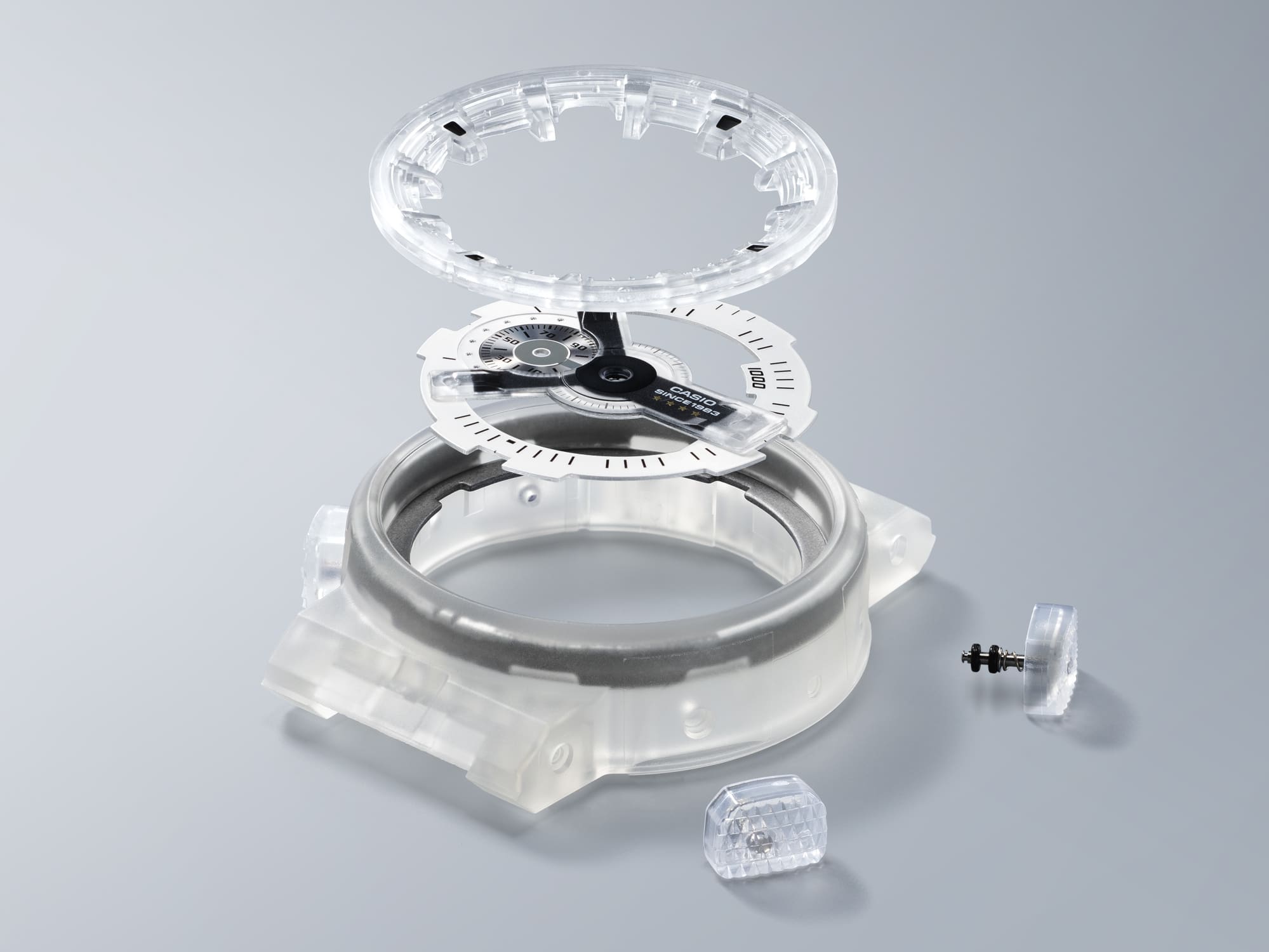 Der durchsichtige Zifferblattring, das Zifferblatt, das transparente Gehäuse und die druchsichtigen Seitenknöpfe der DW-6940RX-7 als Einzelteile übereinander dargestellt