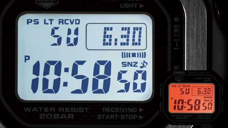 Das Display einer Casio G-Shock GMW-B5000 Digitaluhr im Dunkeln mit hell beleuchtetem Zifferblatt, davor in klein: das Display mit orangener Beleuchtung