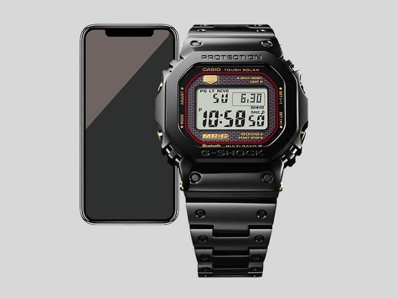 Die schwarze Casio G-Shock MRG-B5000B-1 Bluetooth®-Uhr, dahinter: Ein Smartphone