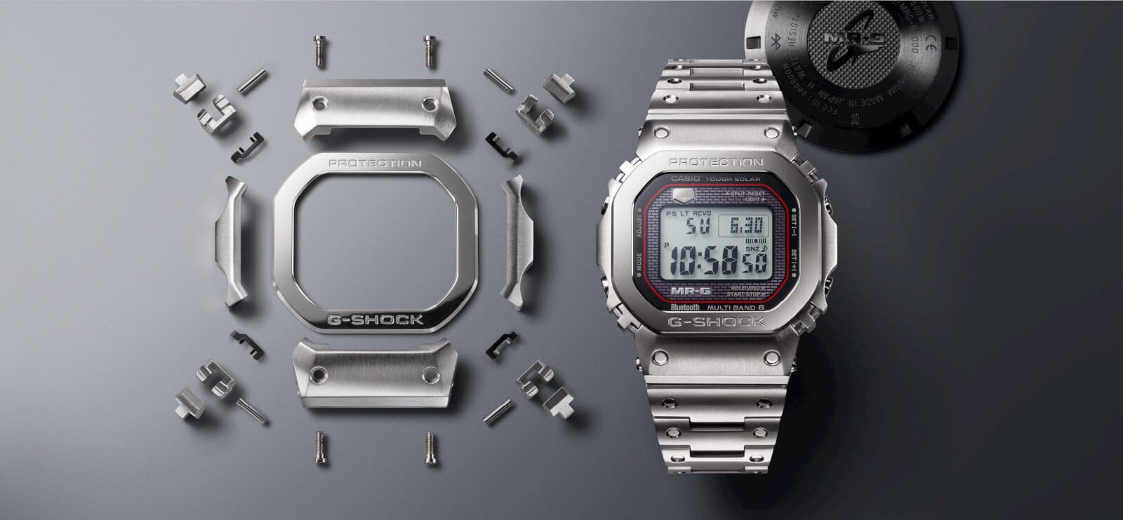 Die silberfarbene MRG-B5000D-1 Digitaluhr neben den Einzelteilen, aus denen ihr Gehäuse zusammengesetzt ist