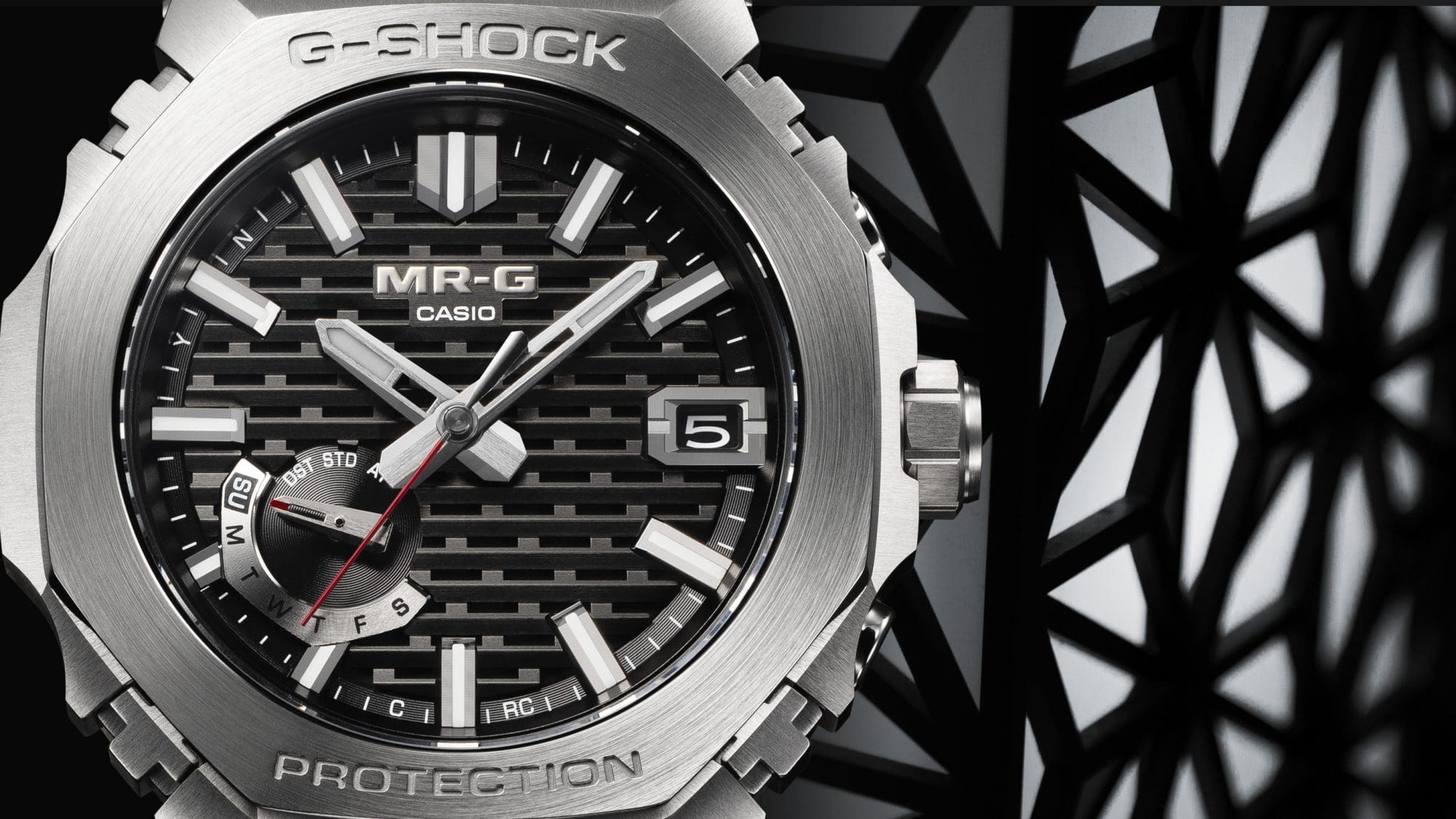 Nahaufnahme des schwarz-gemusterten Zifferblatts der silbernen Casio MRG-B2100D-1A Vollmetalluhr vor geometrischen Schattenmustern