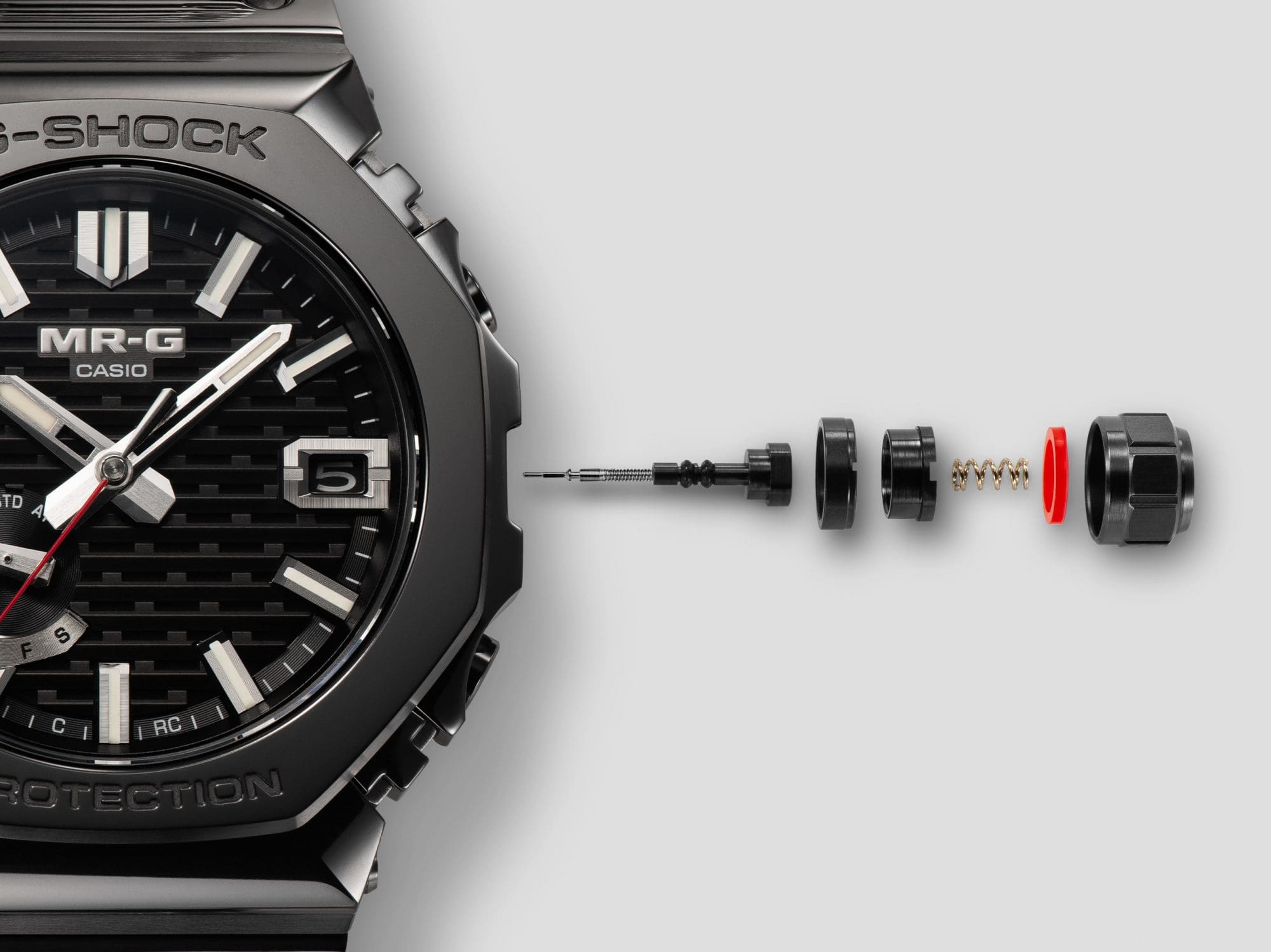 Die einzelnen Komponenten der Kronenkonstruktion neben dem Gehäuse der Armbanduhr MRG-B2100B-1A