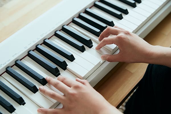 Nahaufnahme: Zwei Hände spielen auf dem weißen CDP-S110WE Klavier. Das Digitalpiano liegt auf einem Holztisch.