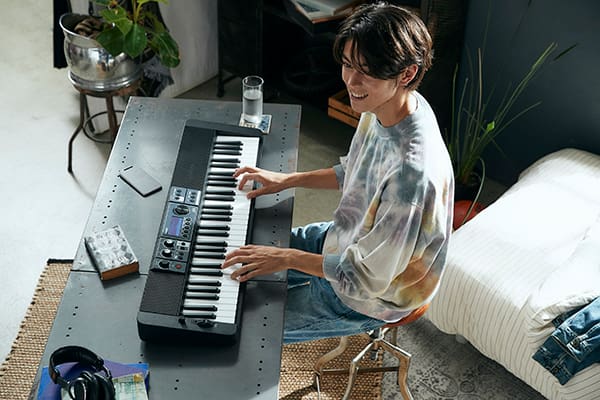 Ein junger Mann spielt gut gelaunt auf einem Casiotone CT-S500, dass in einem Wohnraum auf einem Tisch liegt