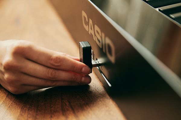 Eine Hand steckt ein MIDI & Audio Adapter ins schwarze Privia PX-S1100BK Digitalpiano von CASIO