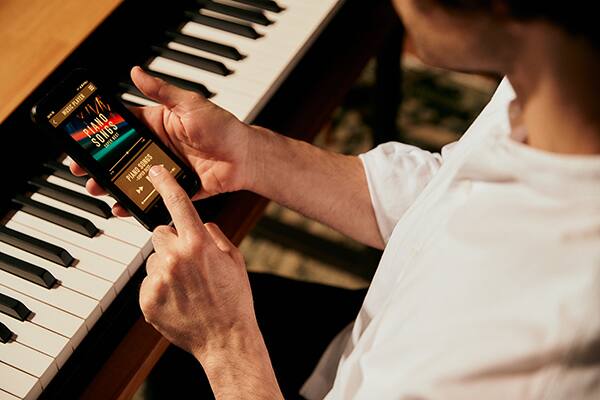 Jemand bedient den Music Player seines Smartphones direkt über der Tastatur eines Privia PX-S5000-Digitalpiano