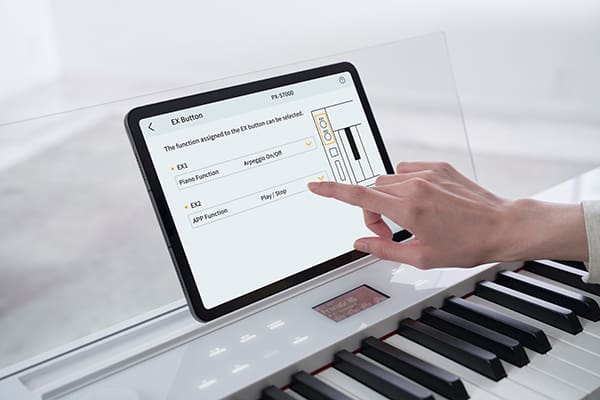Eine Hand berührt ein Tablet, das in der transparenten Notenhalterung des PX-S7000WE Digitalpianos steht, um die "CASIO MUSIC SPACE"-App zu bedienen