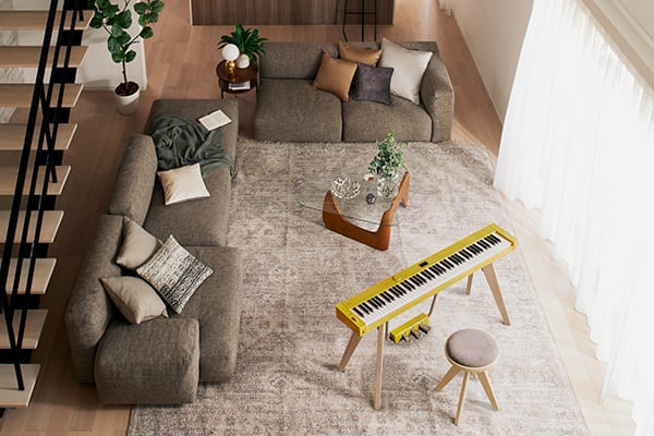 Blick von oben in ein hellen Wohnzimmer und das  Privia PX-S7000HM Digitalpiano auf einem Teppich gegenüber einer Sitzgruppe