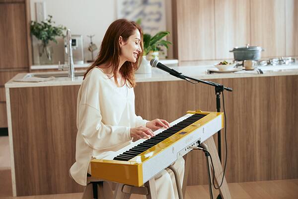 Eine Frau sitzt am PX-S7000HM Digitalpiano, spielt Klavier und singt in ein Mikrofon