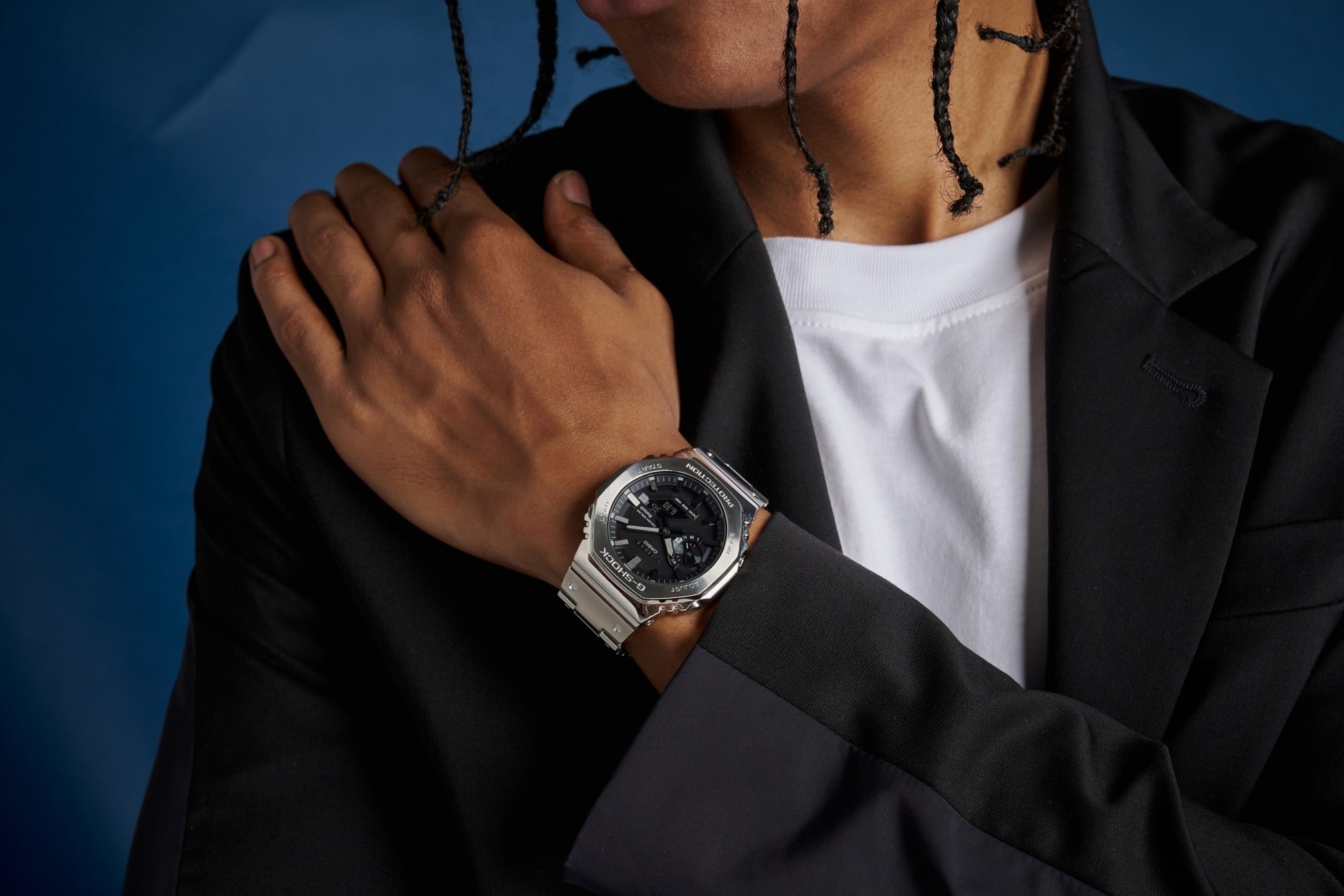 Ein silberner, analog-digitaler Chronograf mit schwarzem Zifferblatt der GM-B2100 Serie am Handgelenk einer Person in dunklem Sakko und weißem T-Shirt