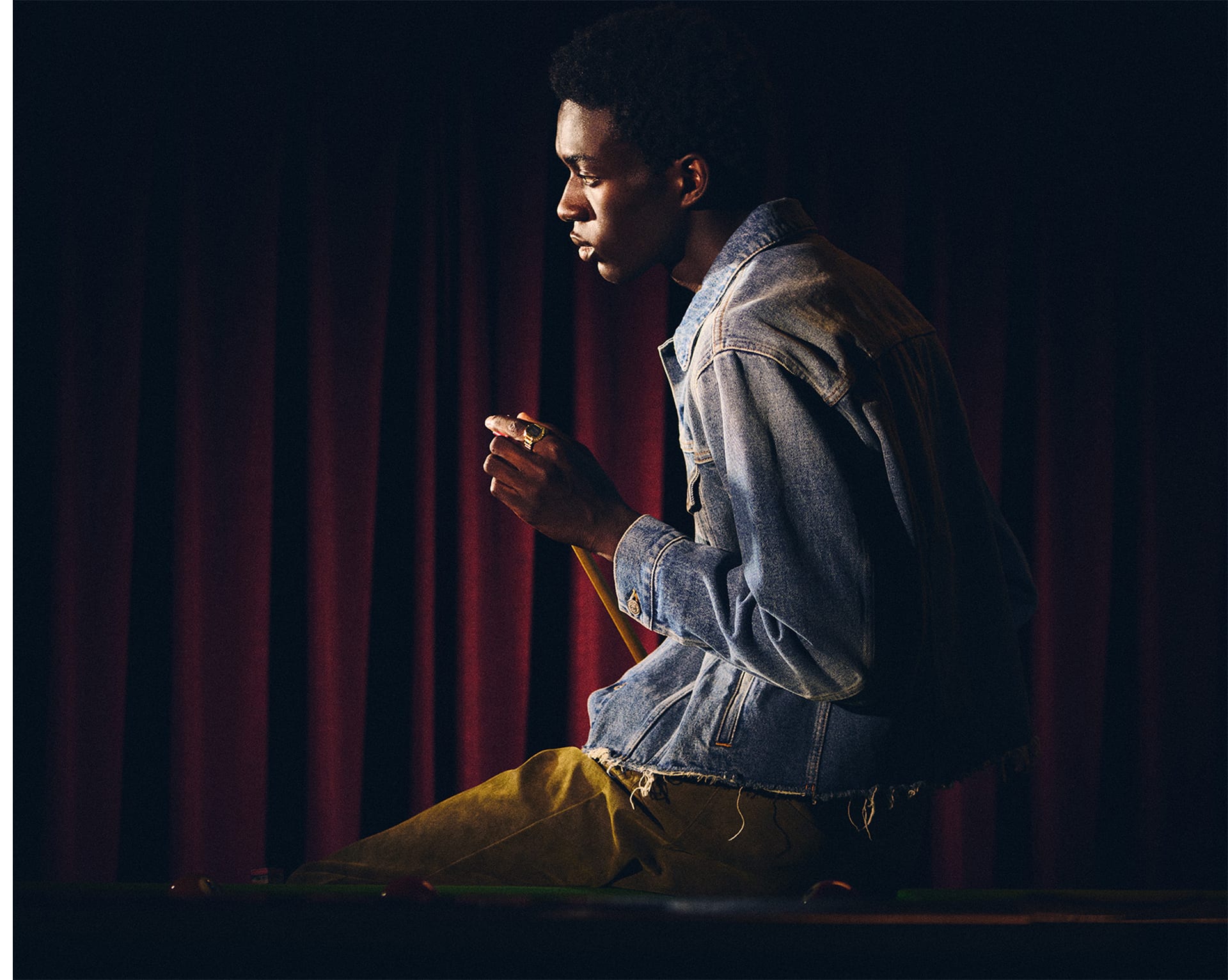 A photo of a man wearing CRW-001G on his finger sitting at a pool table and touching a cue stick.